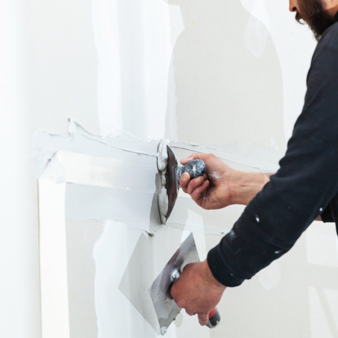 Gentleman repairing drywall in a commercial building using a scraper and spatula.