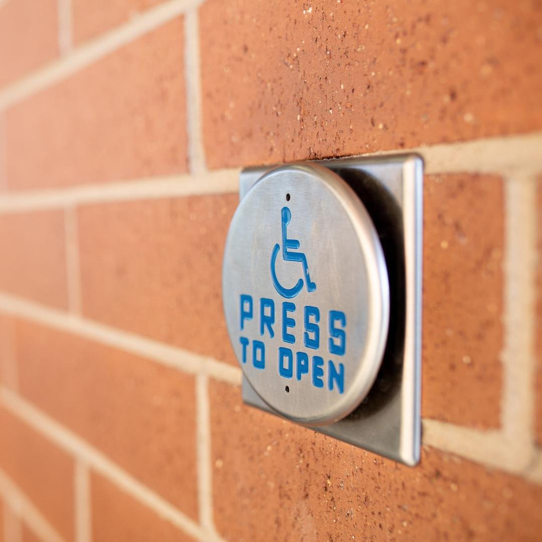 Close-up photo of a blue handicapped access button mounted on a red brick wall.