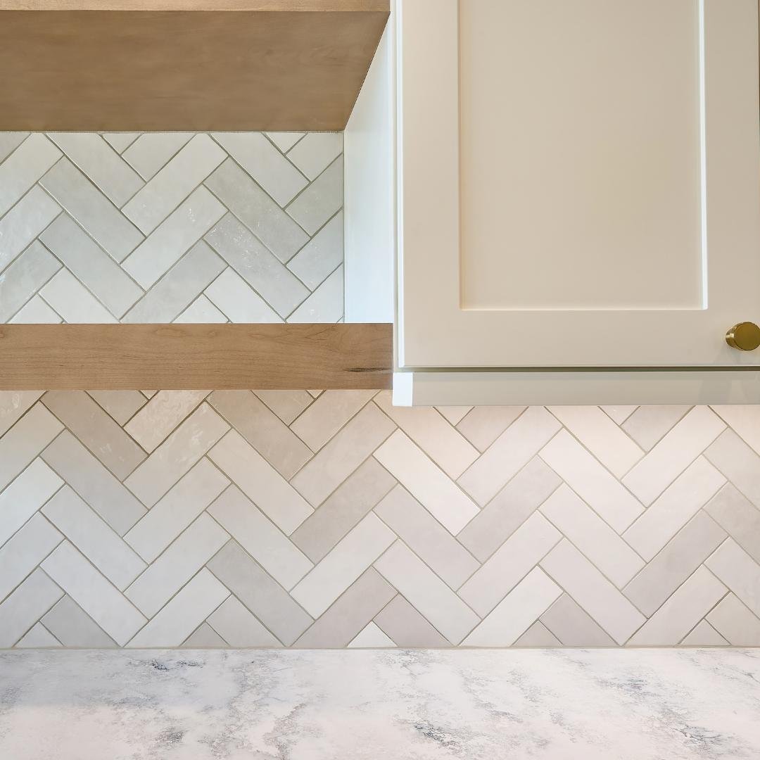 A white herringbone tile backsplash being installed in a kitchen with white cabinets and countertops.