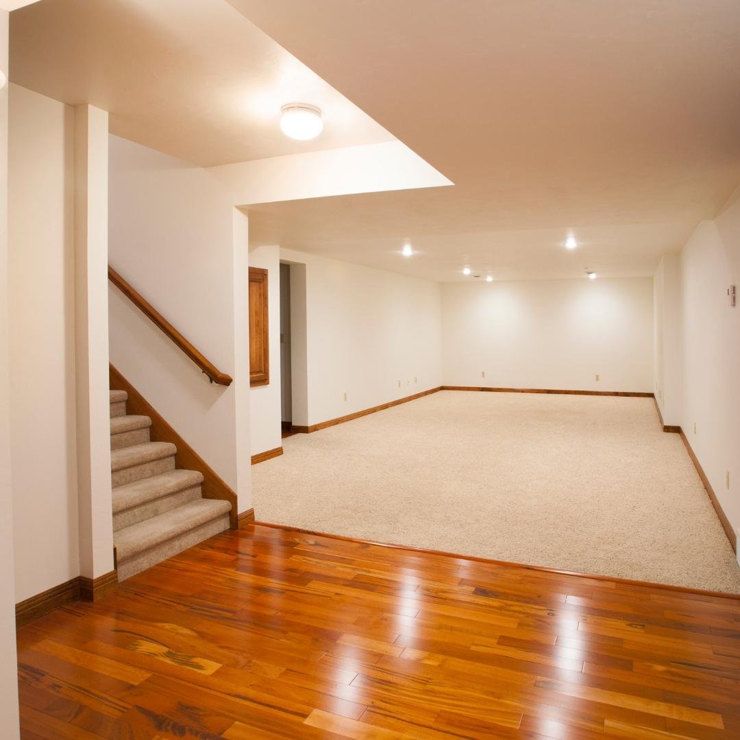 Empty finished basement with hardwood floors and painted white stairs.