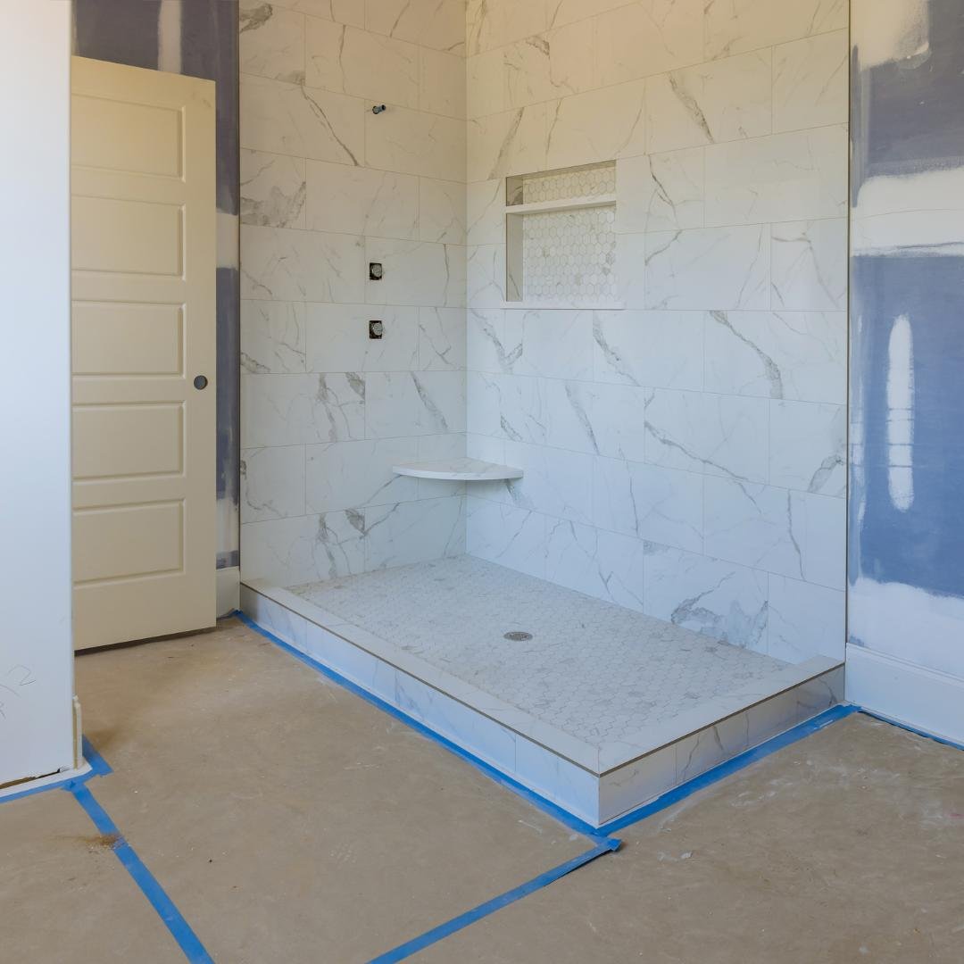 Close-up of bathroom remodel, walk-in shower under construction with marble tile and shelf.