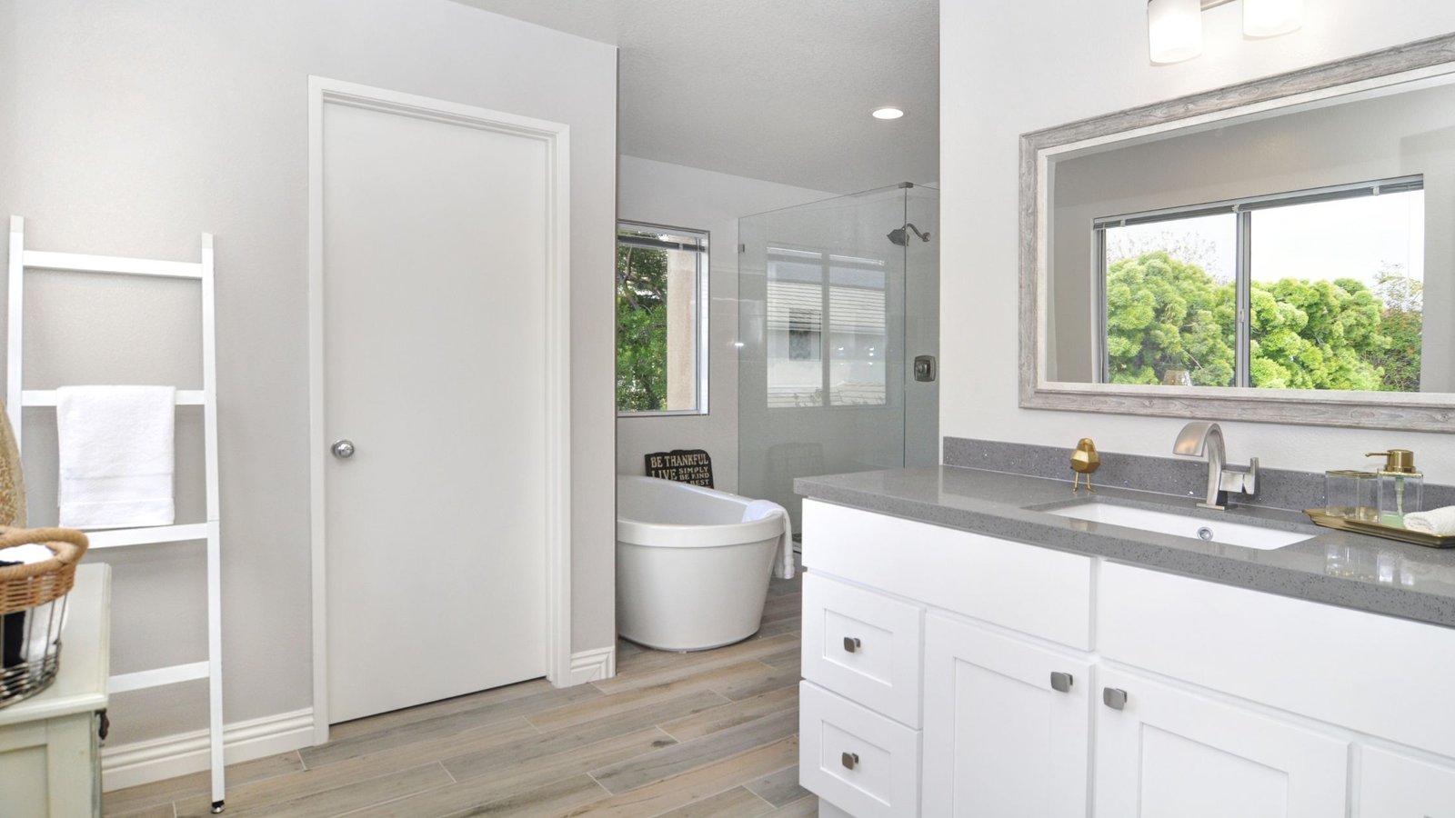 A completely remodeled bathroom with a modern freestanding bathtub, a walk-in shower with glass doors, a double sink vanity with quartz countertops, and light-colored wood cabinets.