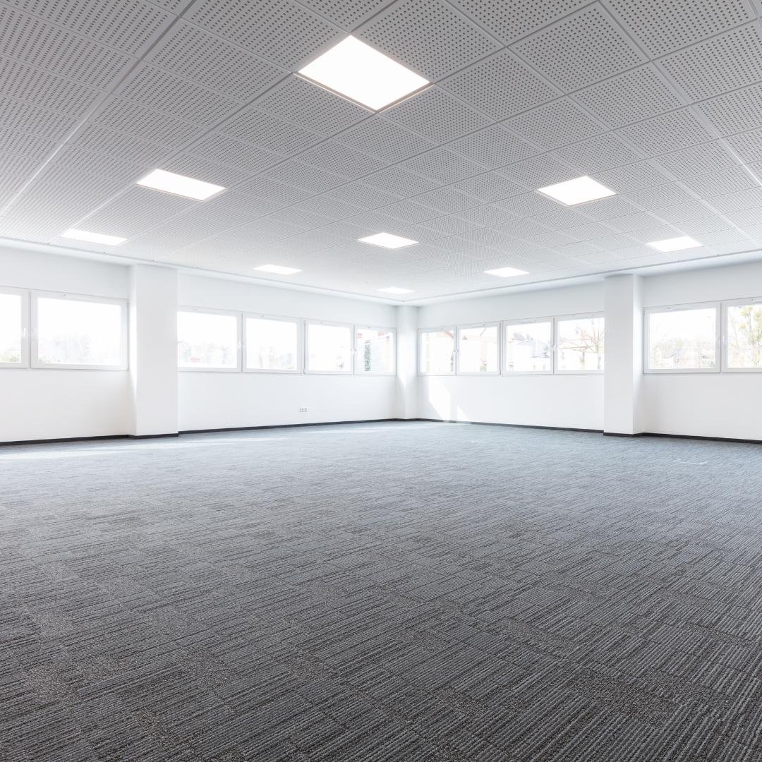 Empty, carpeted room with a finished ceiling and completed white walls, a completed commercial interior demolition and build-out.