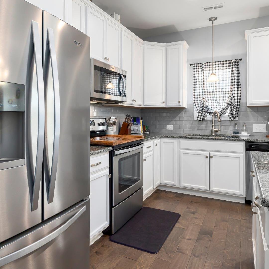 A stainless steel refrigerator, stove, and microwave installed in a kitchen with white cabinets and stainless steel appliances.