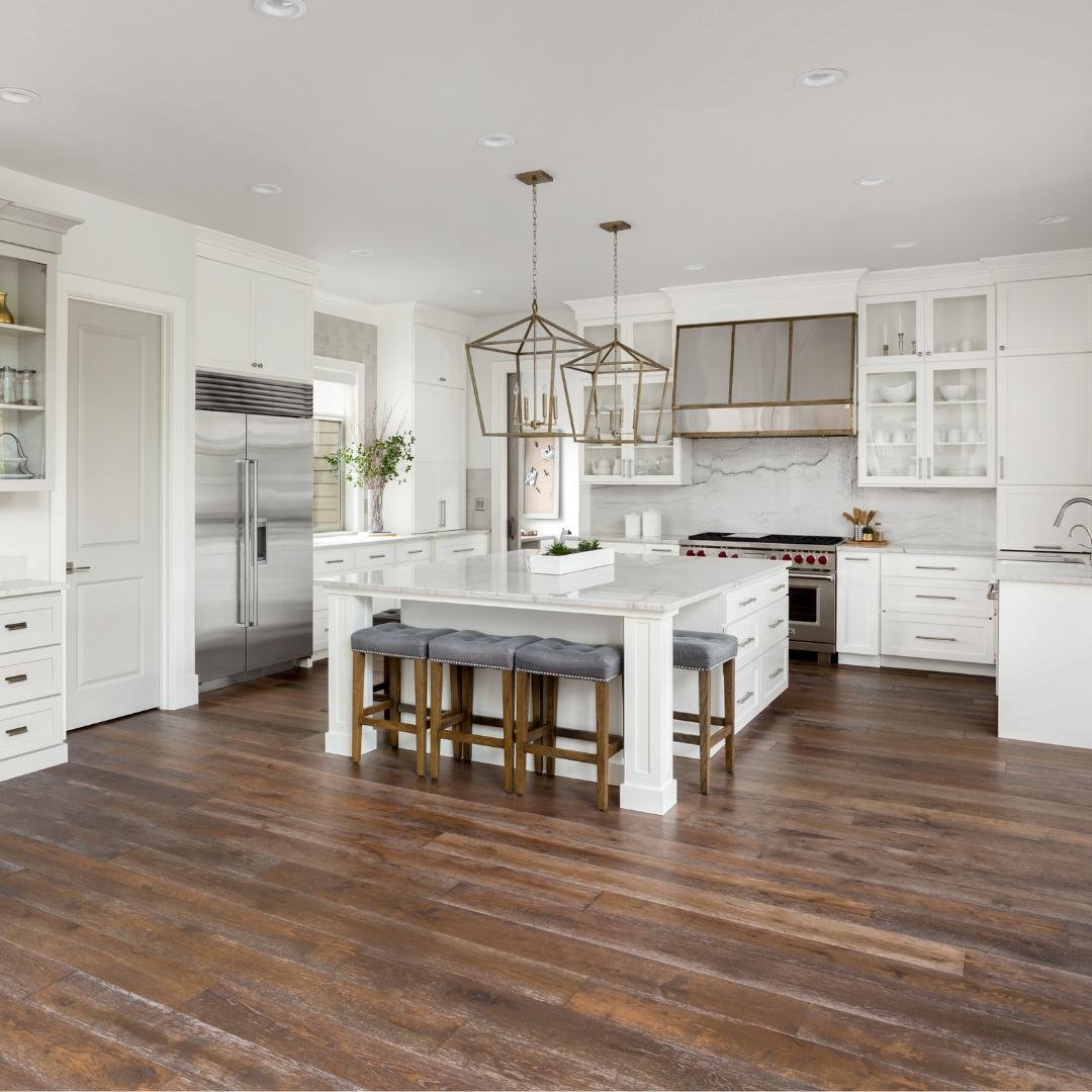 A white marble kitchen counter with a stainless steel sink and faucet in a kitchen with white cabinets and stainless steel appliances and a new dark wood kitchen floor.