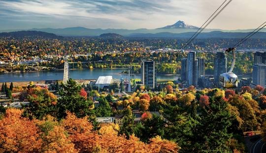 A photo of the Portland, Oregon skyline in fall, with colorful trees in the foreground and snow-capped Mount Hood in the background.