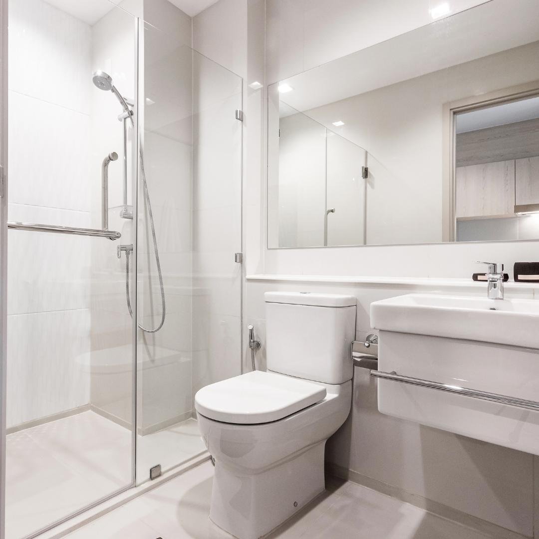 A white, elongated low-profile toilet with a chrome flush lever being installed in a bathroom with a gray tile floor.