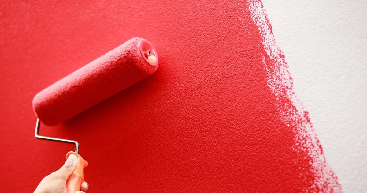 Red paint roller applying red paint to a white wall.